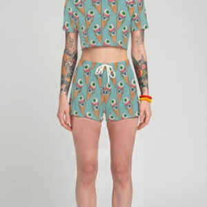 A model with pastel lavender hair wearing a pink two-piece pastel goth outfit, featuring a short-sleeve crop top and matching shorts with a seamless pattern of melting eyeball ice cream cones.